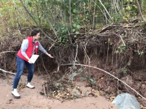 Lydia Salus holds a checklist and points out tilted trees and a groundwater seep in the bluff.