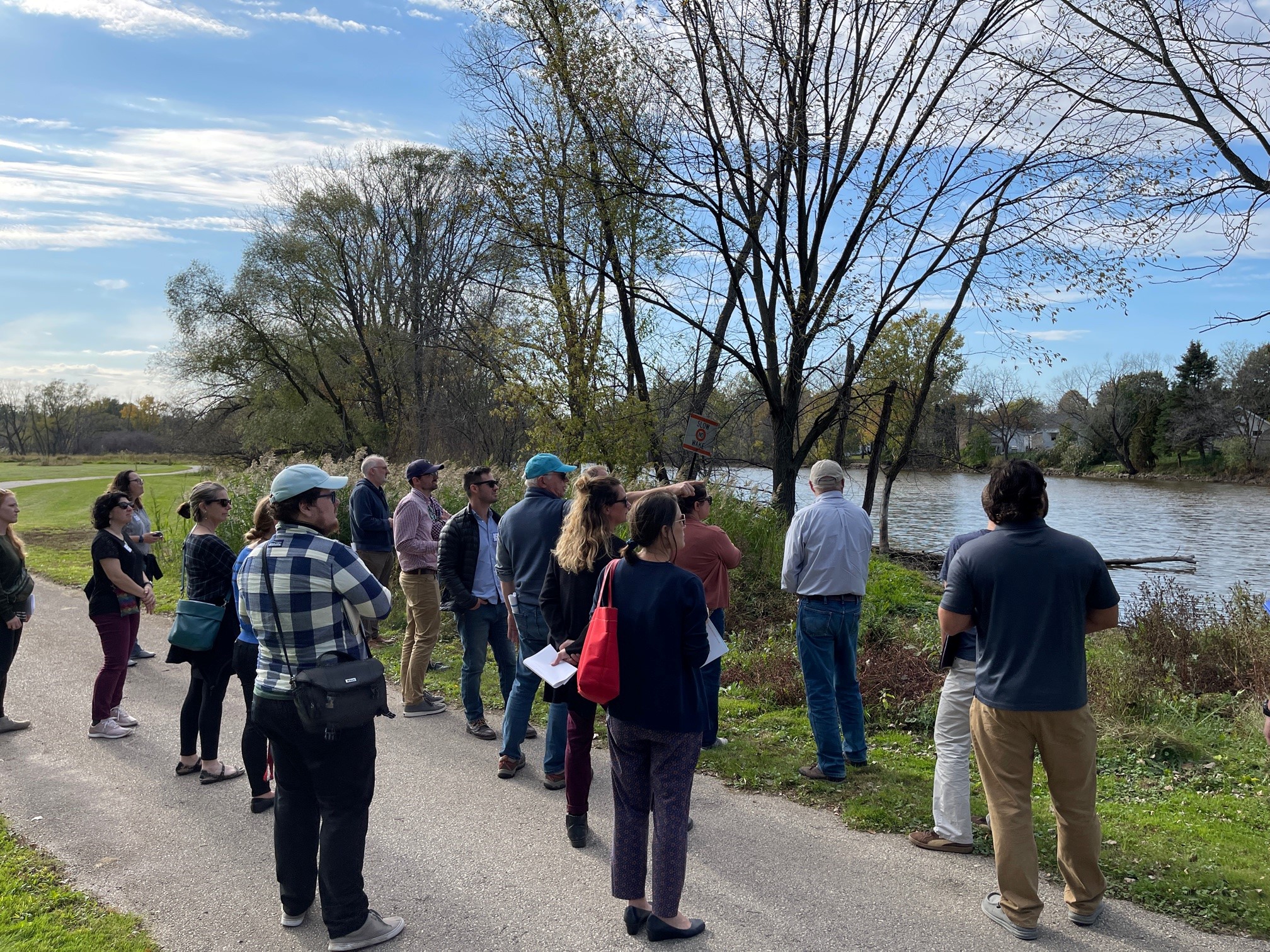 A group of people stand on a paved path alongside the East River in Green Bay near the site of worst flooding in 2019