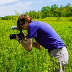 Abbie Brown looks through a camera while standing in a marshy area