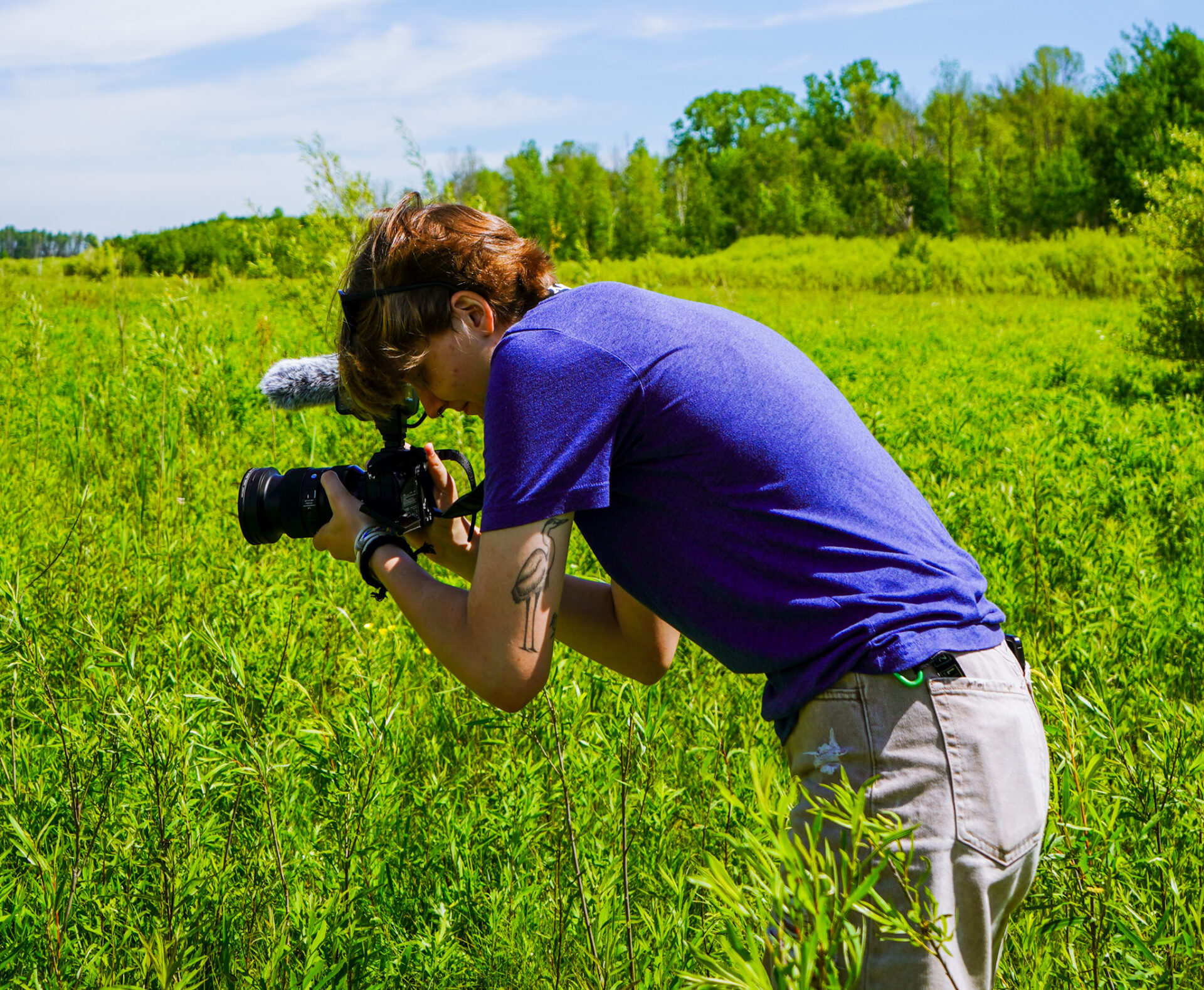 Abbie Brown looks through a camera while standing in a marshy area