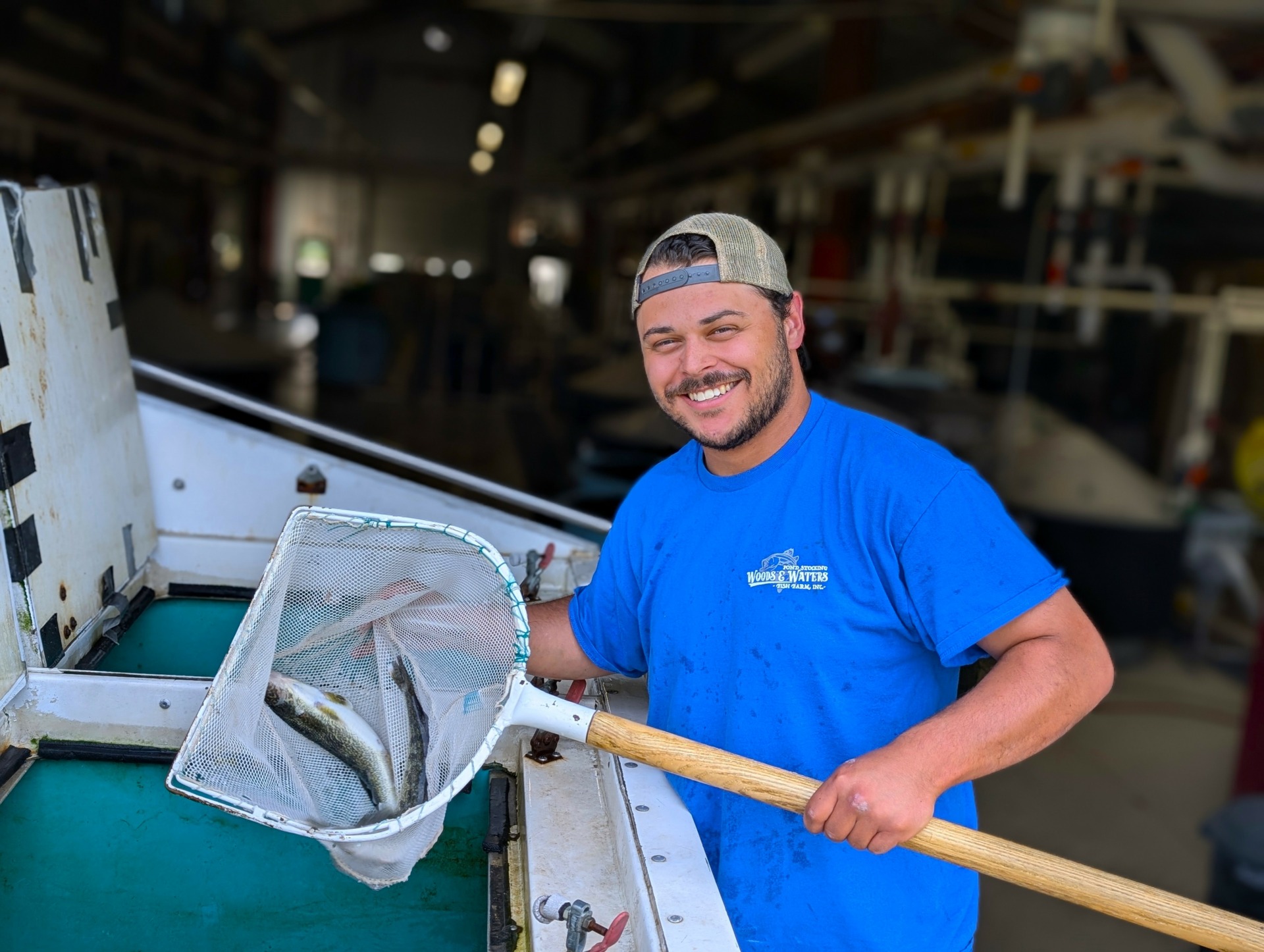 A man in a blue t-shirt holds up two walleye in a net