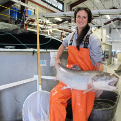 A woman in orange waders holds a large Atlantic salmon