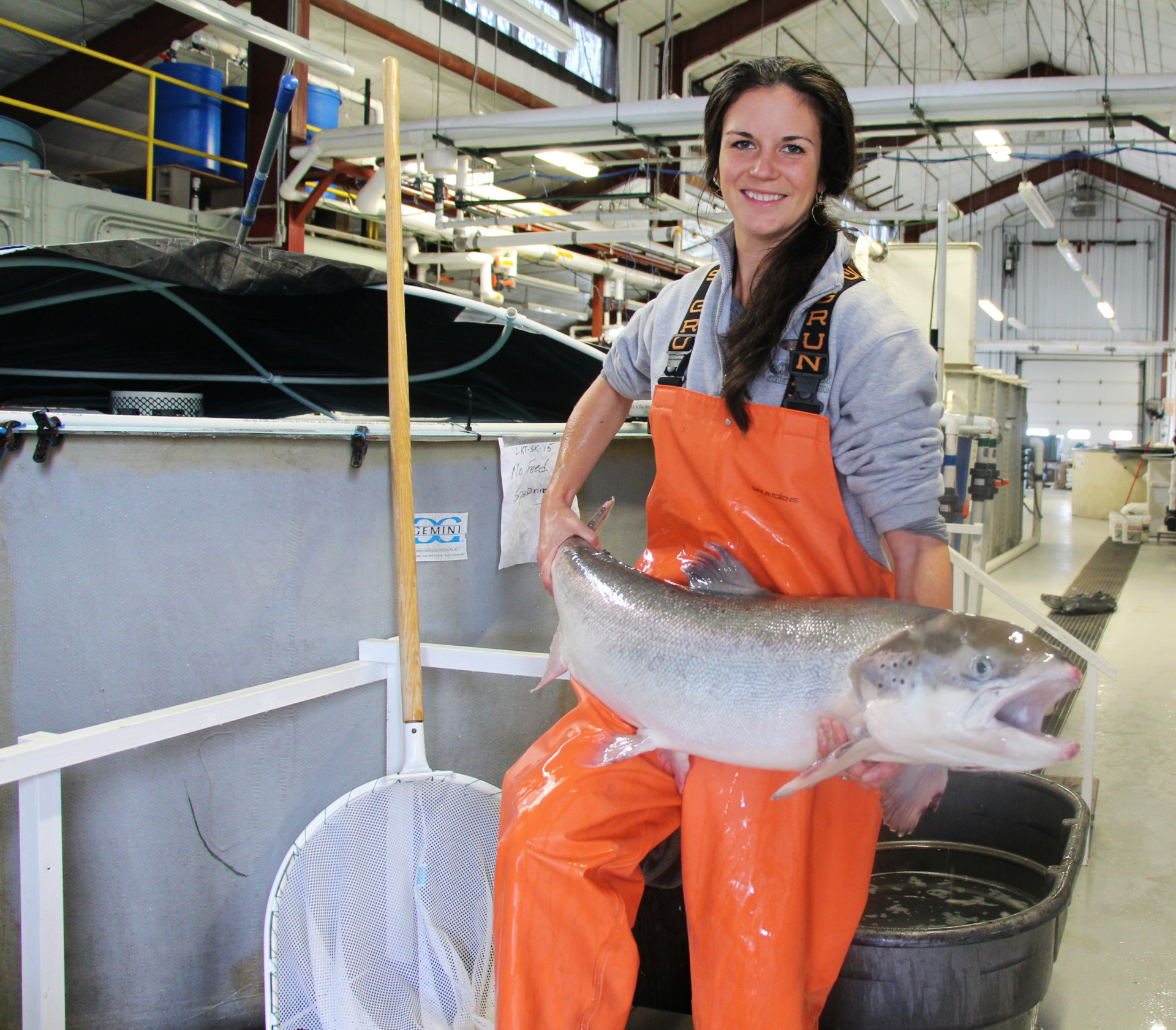 A woman in orange waders holds a large Atlantic salmon