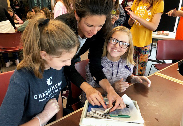 Aquaculture outreach specialists Emma Hauser helps two smiling kids with a fish dissection