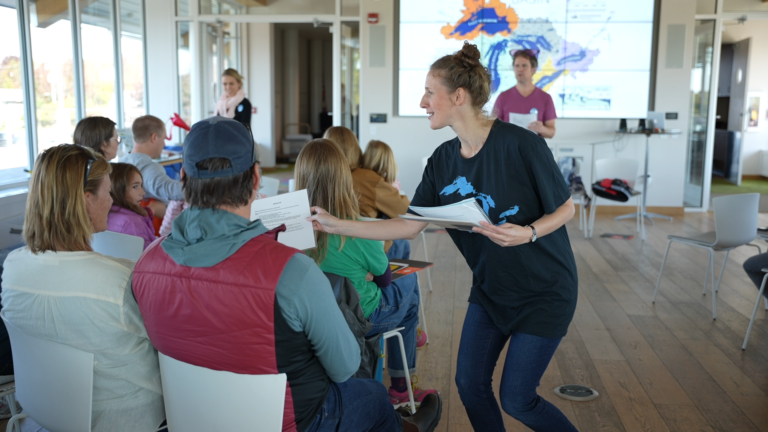 A woman handing out papers to people who are seated.