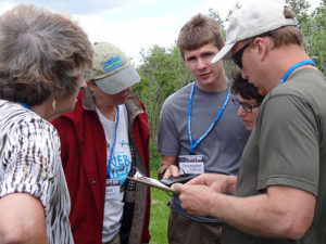 People gathered around a clipboard outdoors in the woods.