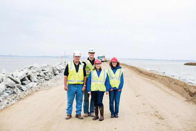 Four people standing by a lake wearing hard hats and yellow vests