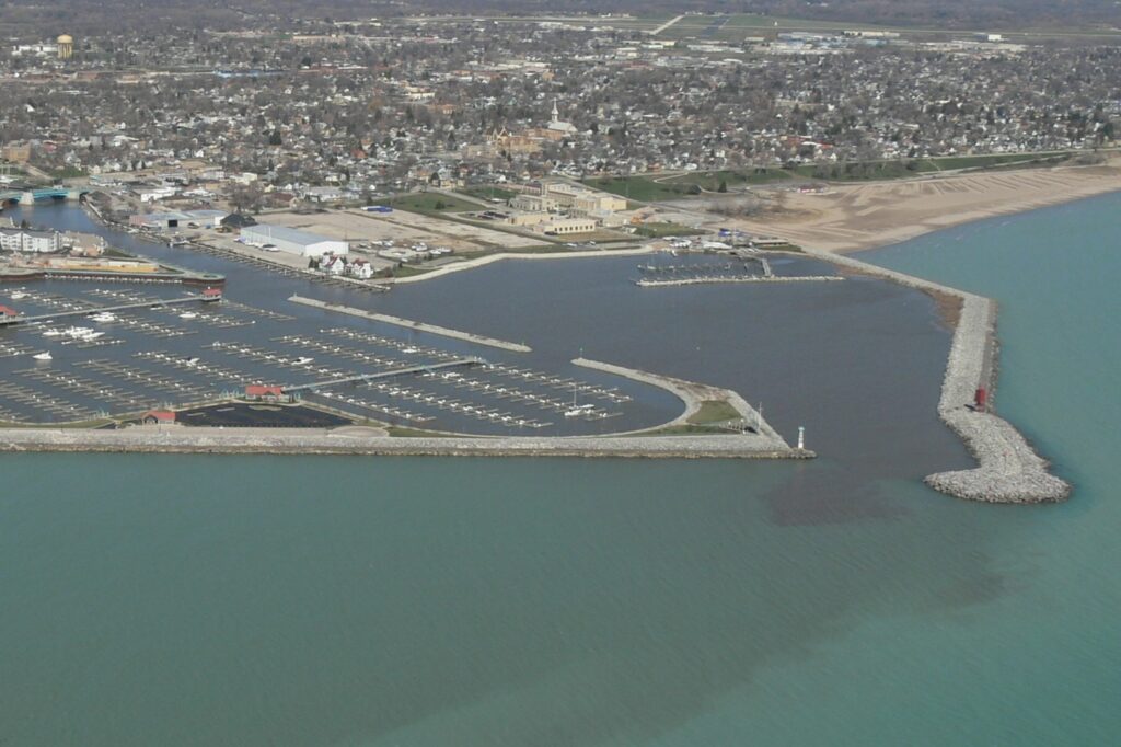 Aerial photograph of Racine Harbor in 2007. Two breakwaters (the south and north breakwater) extend out from the shoreline into Lake Michigan from approximately 1/4 mile to either side of the Root River. The area immediately adjacent to the south breakwater is now home to the large Reef Point Marina. This marina, with its multiple rows of docks, provides slips to house hundreds of boats.